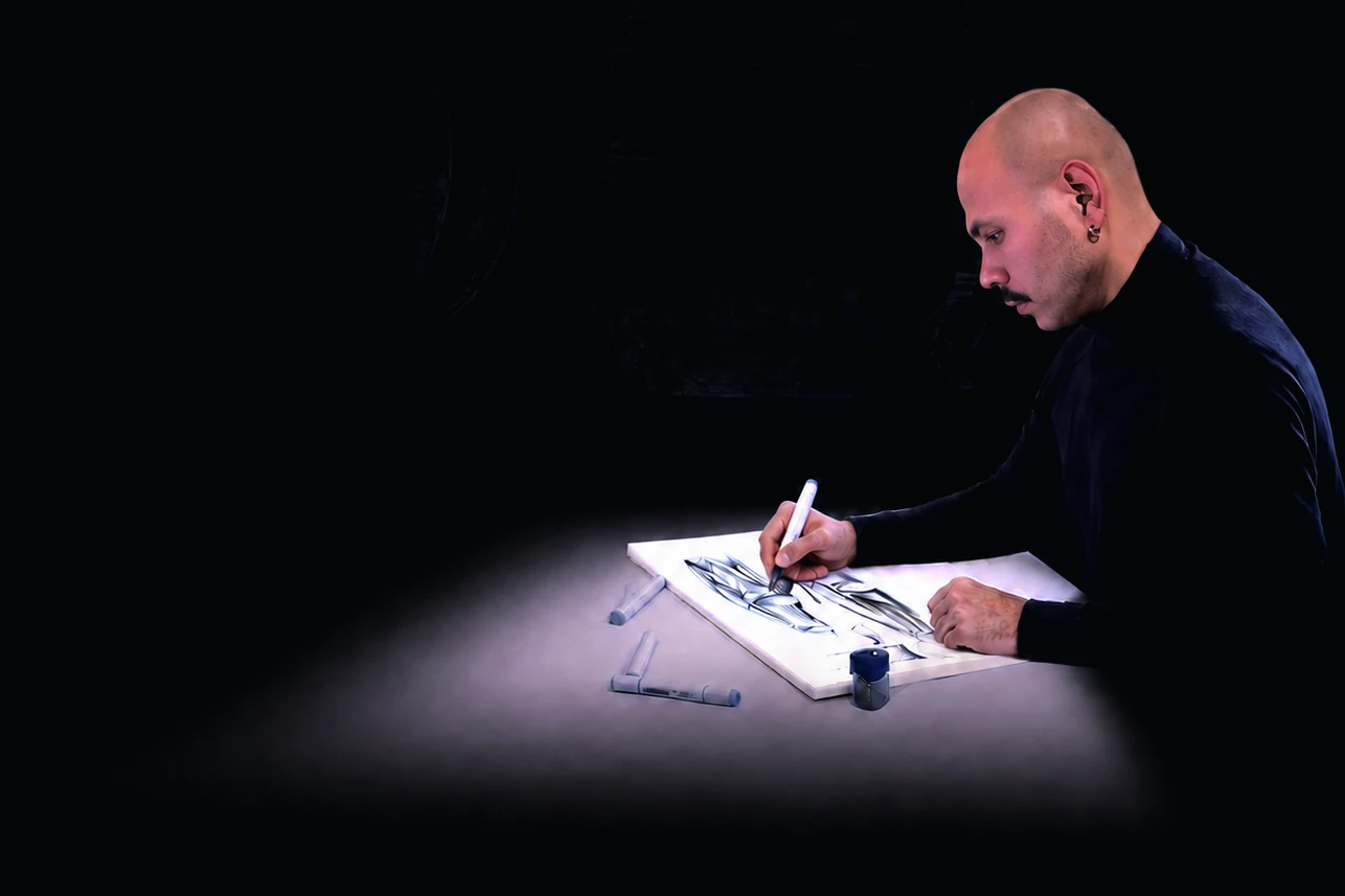 Elschad Abylov sketching with a marker under a desk lamp